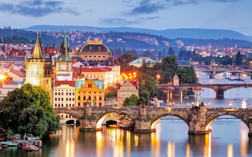 Evening view of Charles Bridge and Vltava River in Prague with illuminated cityscape.