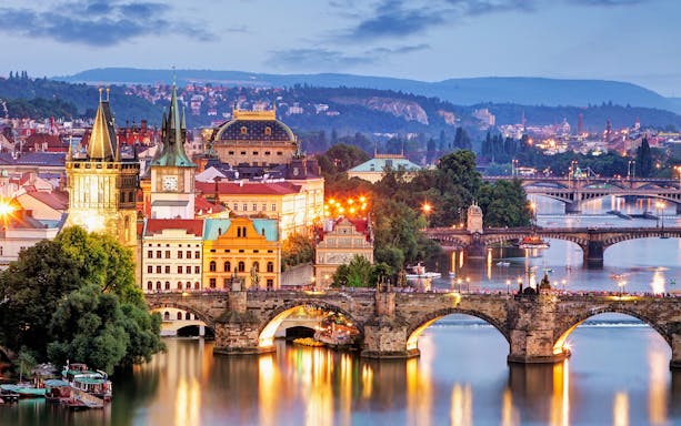 Evening view of Charles Bridge and Vltava River in Prague with illuminated cityscape.