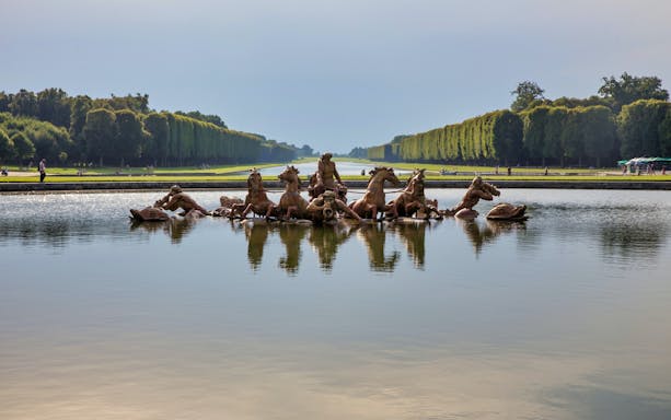 Fountain of Apollo in Versailles Gardens, France, with tree-lined paths in the background.