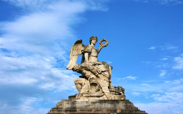 Statue of an angel holding a wreath at Versailles, France, under a blue sky.