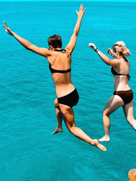 Two people jumping off a boat into the sea during a day cruise from Athens to Agistri, Moni, and Aegina.