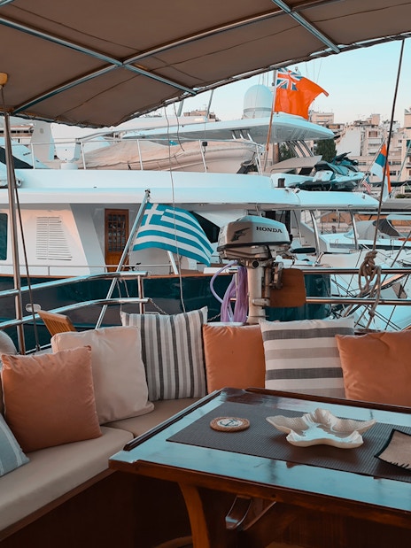 Cozy yacht deck with seating area in Athens marina, Greek flag visible, part of day cruise to Agistri, Moni, Aegina.