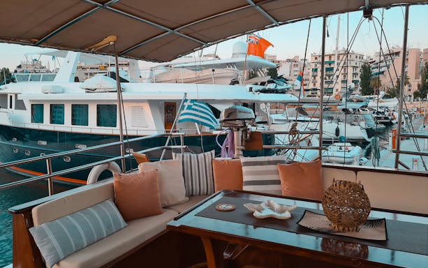 Cozy yacht deck with seating area in Athens marina, Greek flag visible, part of day cruise to Agistri, Moni, Aegina.