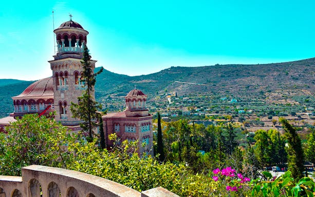 Church with domes and arches on Athens Riviera hillside during night cruise.