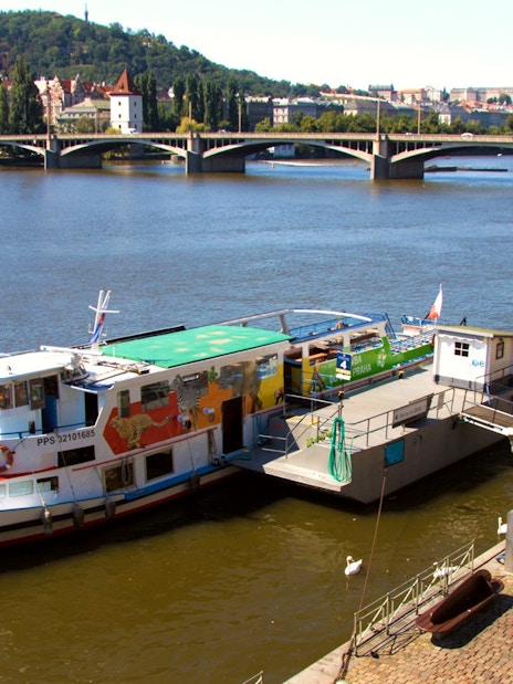 River cruise boat docked on the Vltava River in Prague with passengers boarding.