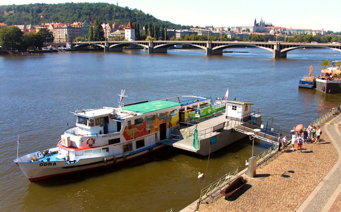 River cruise boat docked on the Vltava River in Prague with passengers boarding.