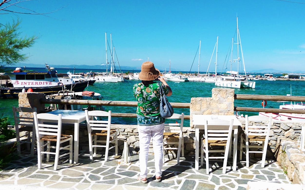 Tourist photographing boats at Aegina harbor during day trip from Athens.