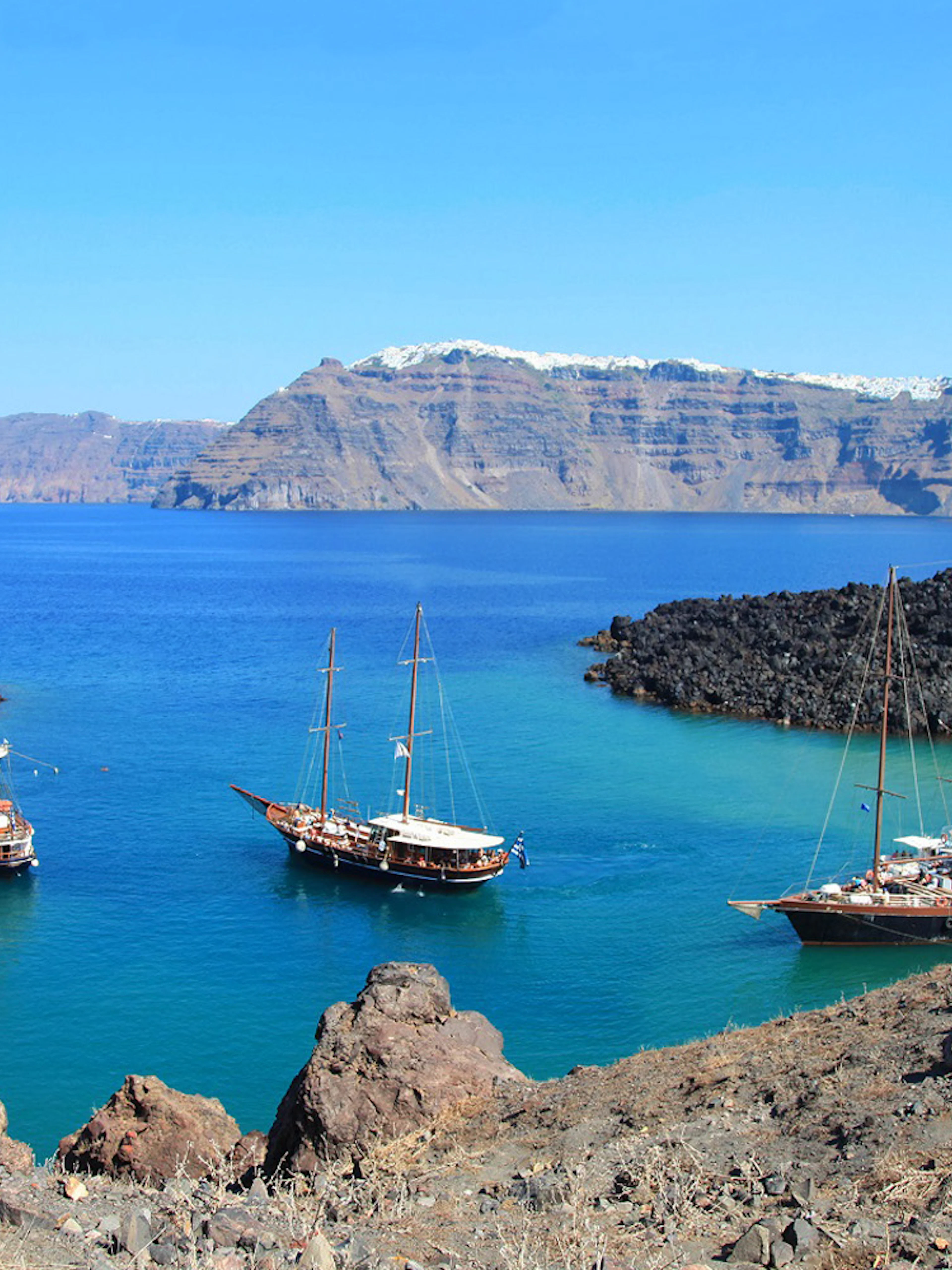 Boats anchored near volcanic rocks on Santorini Volcano Boat Tour.