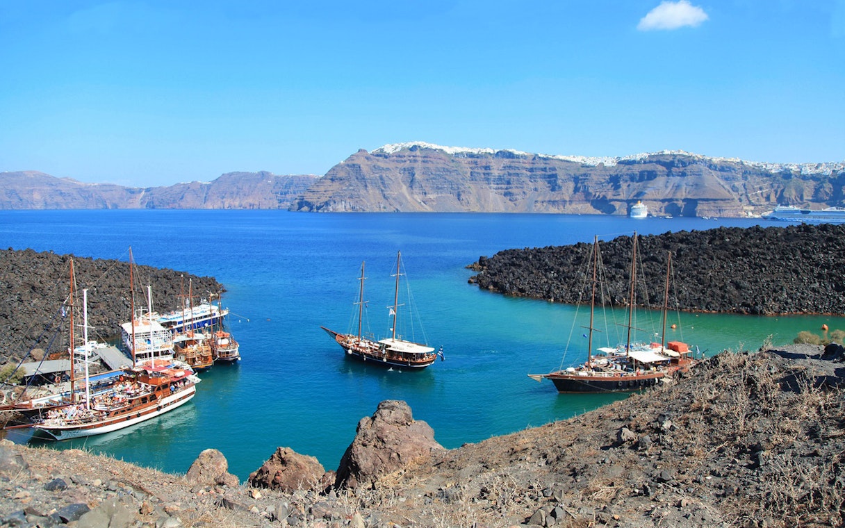 Boats anchored near volcanic rocks on Santorini Volcano Boat Tour.