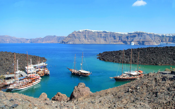 Boats anchored near volcanic rocks on Santorini Volcano Boat Tour.