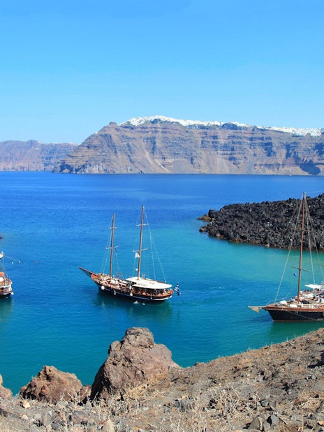 Boats anchored near volcanic rocks on Santorini Volcano Boat Tour.