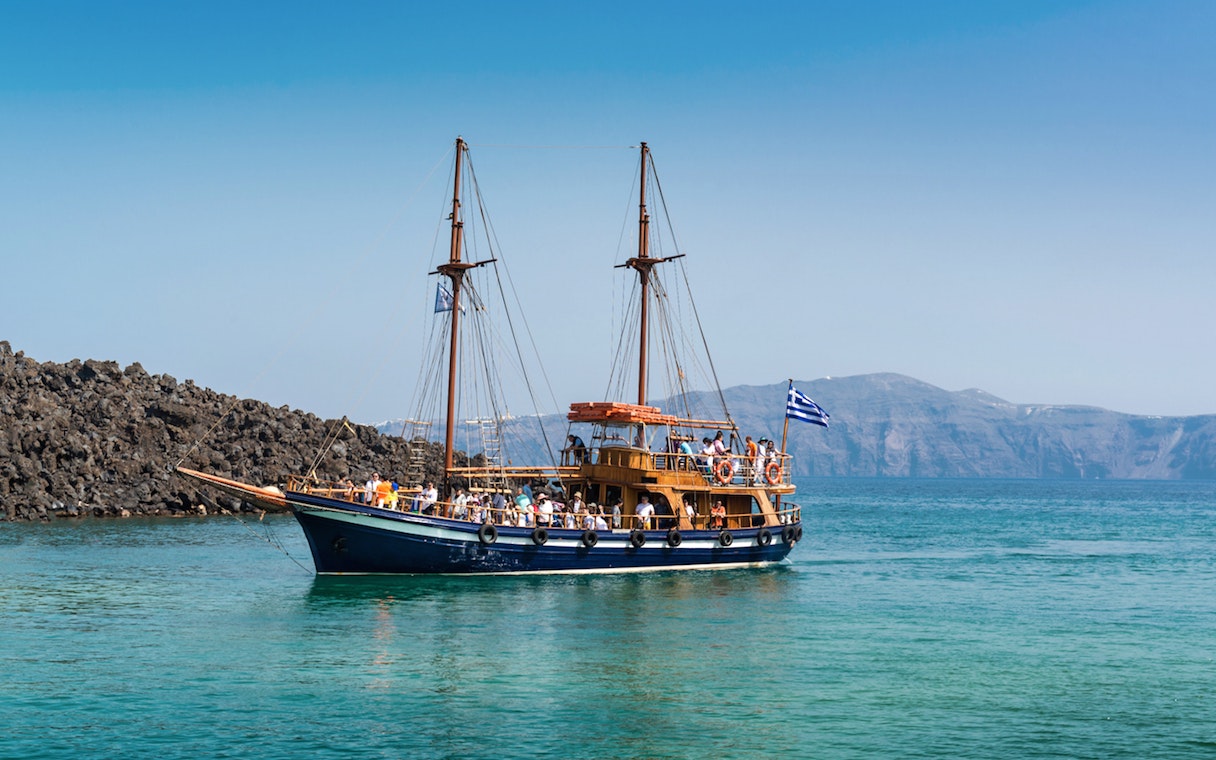 Traditional boat near Santorini volcano with tourists on board.