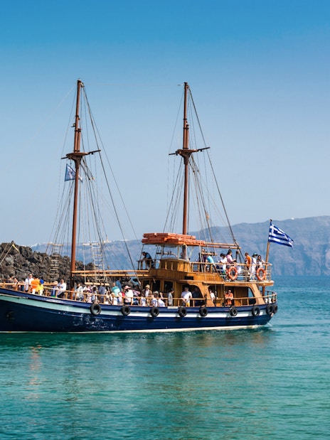 Traditional boat near Santorini volcano with tourists on board.