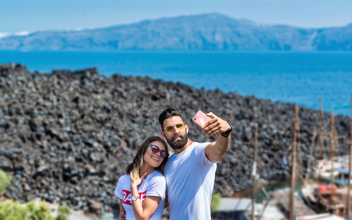 Couple taking selfie on Santorini Volcano boat tour with caldera view.