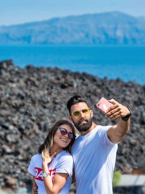 Couple taking selfie on Santorini Volcano boat tour with caldera view.