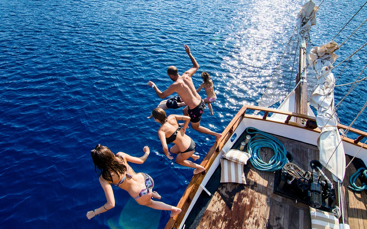 Group jumping off boat into Aegean Sea during Santorini sunset cruise.