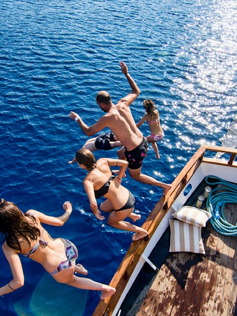 Group jumping off boat into Aegean Sea during Santorini sunset cruise.