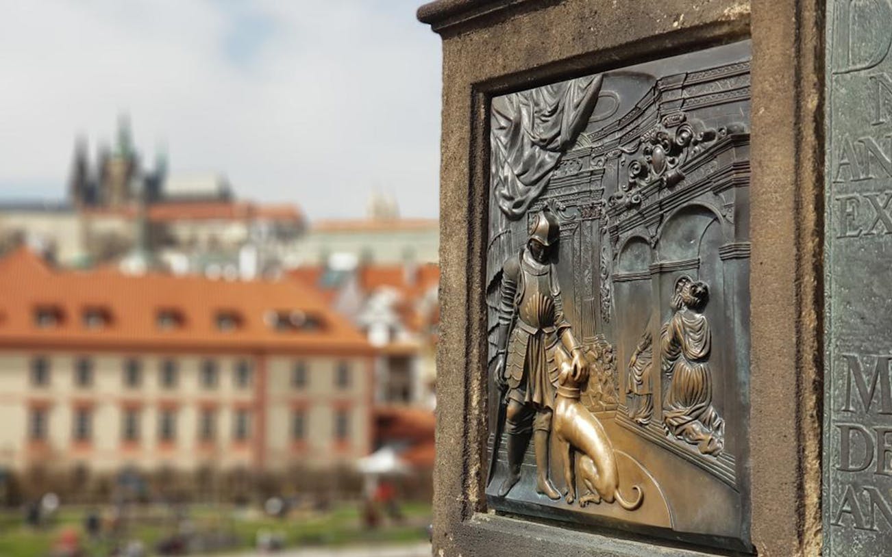 Bronze relief on Charles Bridge with Prague Castle in the background.