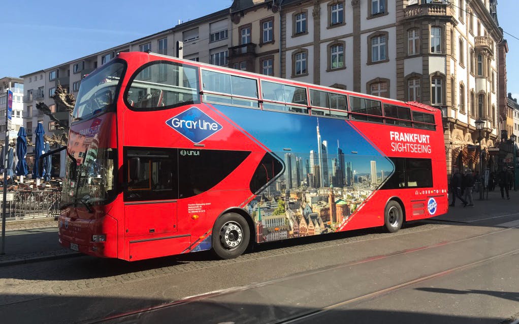 Red double-decker bus for Frankfurt sightseeing tour parked on city street.