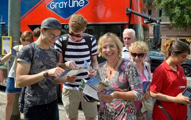 Tourists with maps boarding a red hop-on hop-off bus for the Express Circle City Tour.