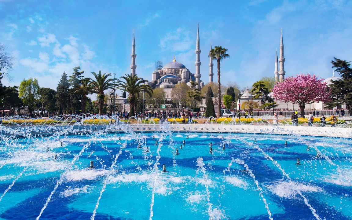 Fountain in front of the Blue Mosque, Istanbul, with minarets and gardens.