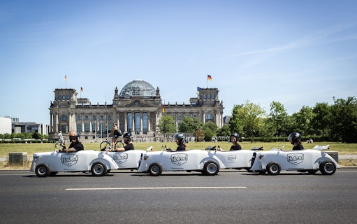 Hot rod cars driving past the Reichstag building in Berlin during a tour.