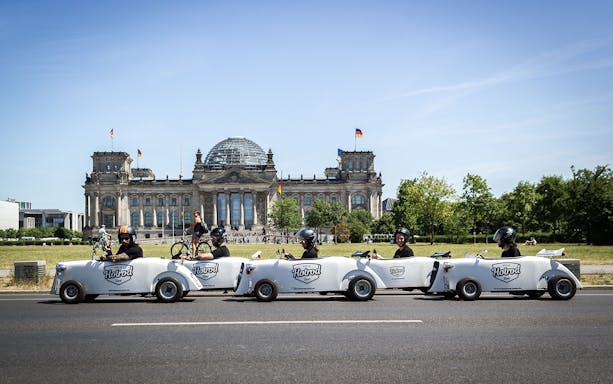 Hot rod cars driving past the Reichstag building in Berlin during a tour.