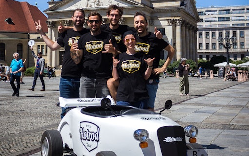 Group posing with hot rod vehicle in Berlin plaza during Hot Rod Tour.