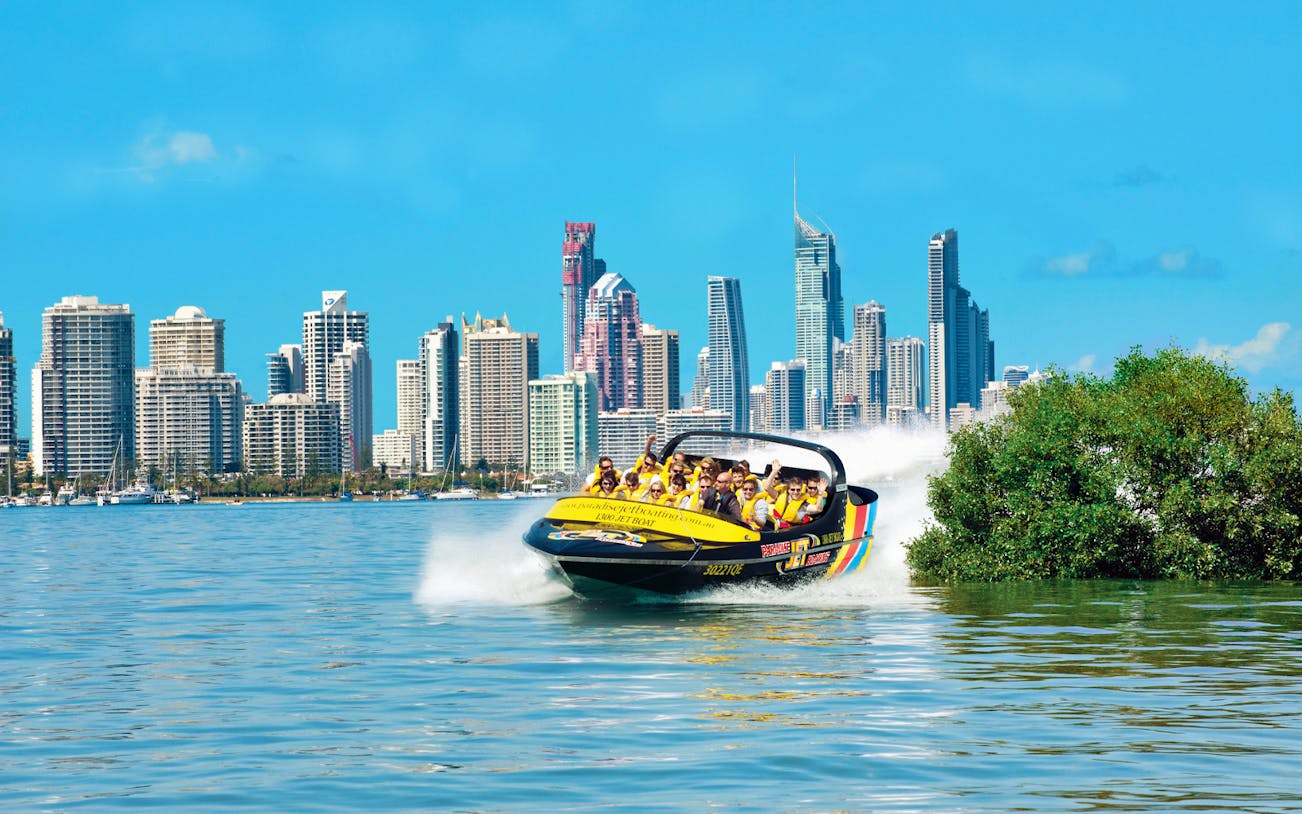 Jet boat speeding on water with city skyline in the background, part of Jet Boating & Jet Ski Circuit Combo.