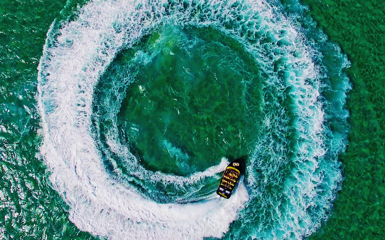 Jetboat creating circular wake on turquoise water, part of a jetboating and parasailing combo.