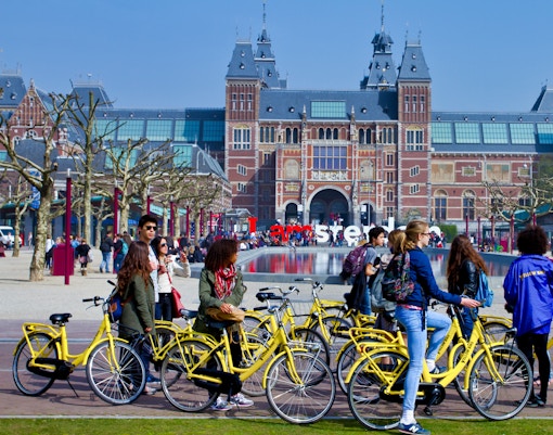 Cyclists on yellow bikes in front of the Rijksmuseum, Amsterdam during a guided tour.