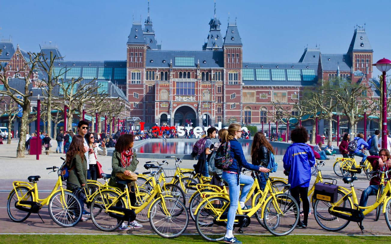 Cyclists on yellow bikes in front of the Rijksmuseum, Amsterdam during a guided tour.