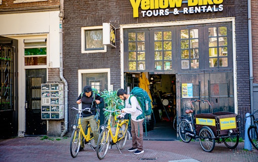 Two people preparing for a guided sightseeing bike tour outside Yellow Bike Tours in Amsterdam.