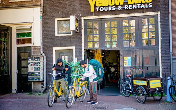 Two people preparing for a guided sightseeing bike tour outside Yellow Bike Tours in Amsterdam.