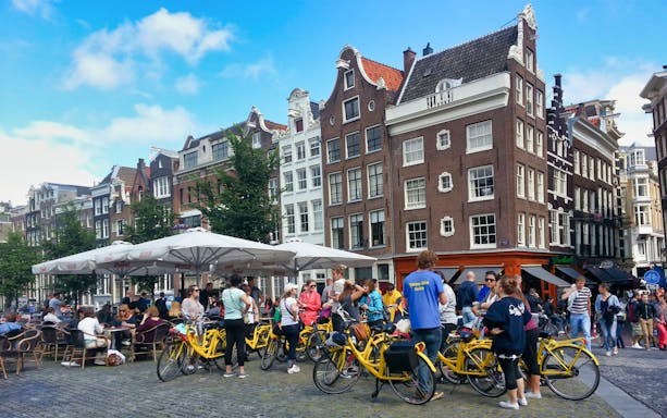 Small group on yellow bikes in Amsterdam's historic district during a guided sightseeing tour.