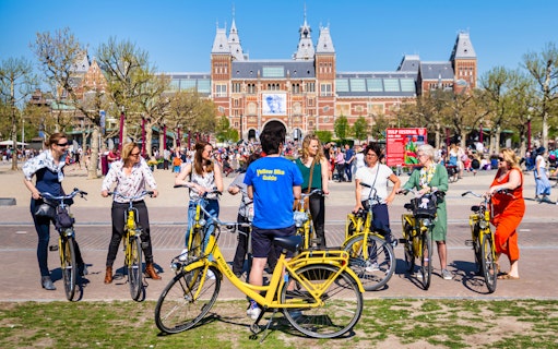 Small group on yellow bikes with guide in front of Rijksmuseum, Amsterdam.