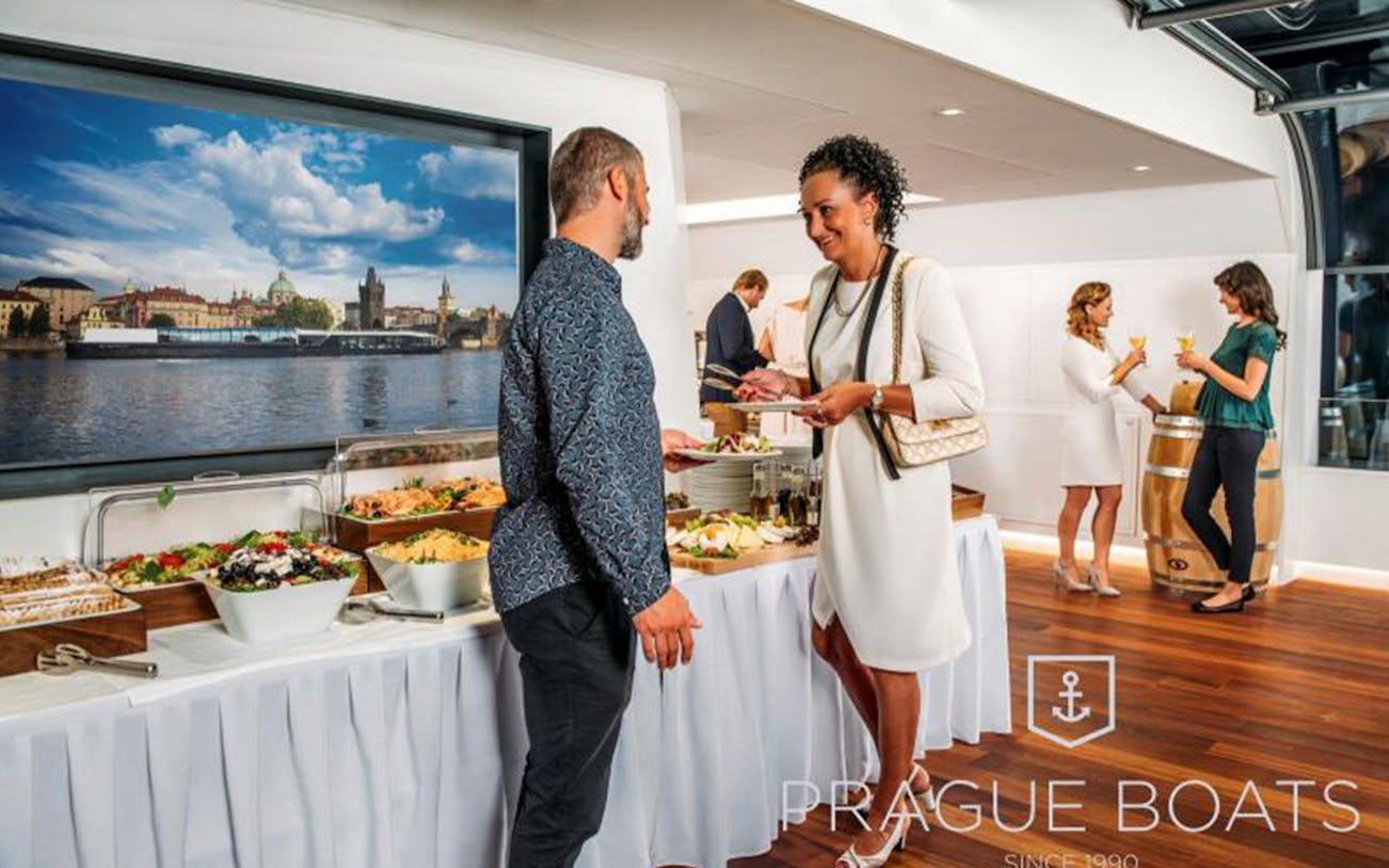 Guests enjoying a buffet on a Prague dinner cruise with cityscape view.