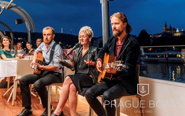 Musicians performing on a Prague dinner cruise with city lights in the background.