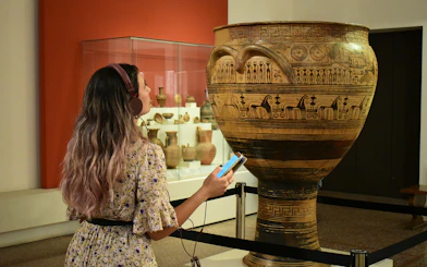 Visitor using audio guide at National Archaeological Museum, viewing ancient Greek pottery.
