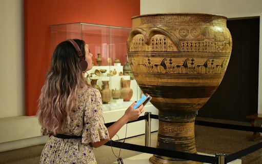 Visitor using audio guide at National Archaeological Museum, viewing ancient Greek pottery.