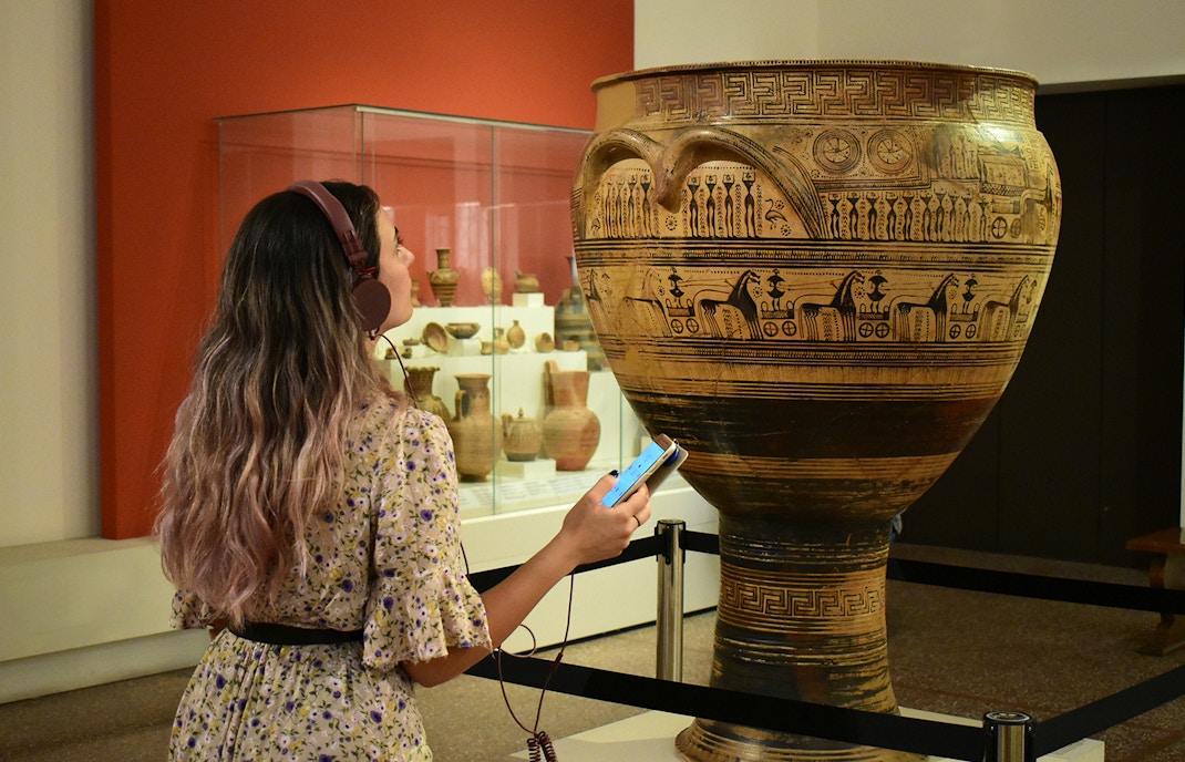 Visitor using audio guide at National Archaeological Museum, viewing ancient Greek pottery.