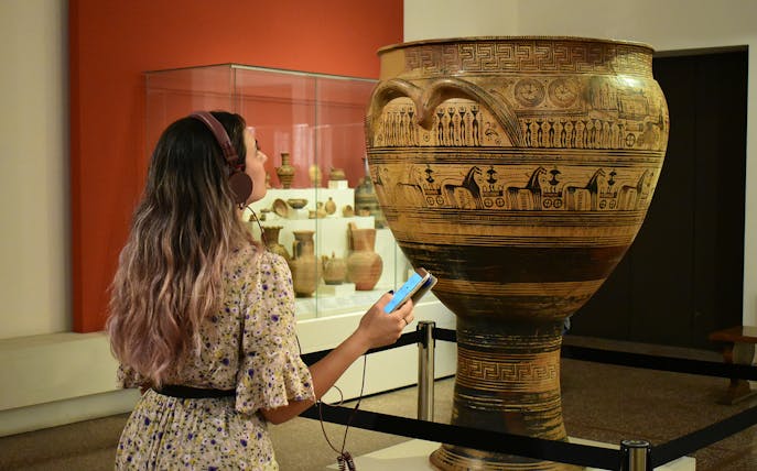 Visitor using audio guide at National Archaeological Museum, viewing ancient Greek pottery.