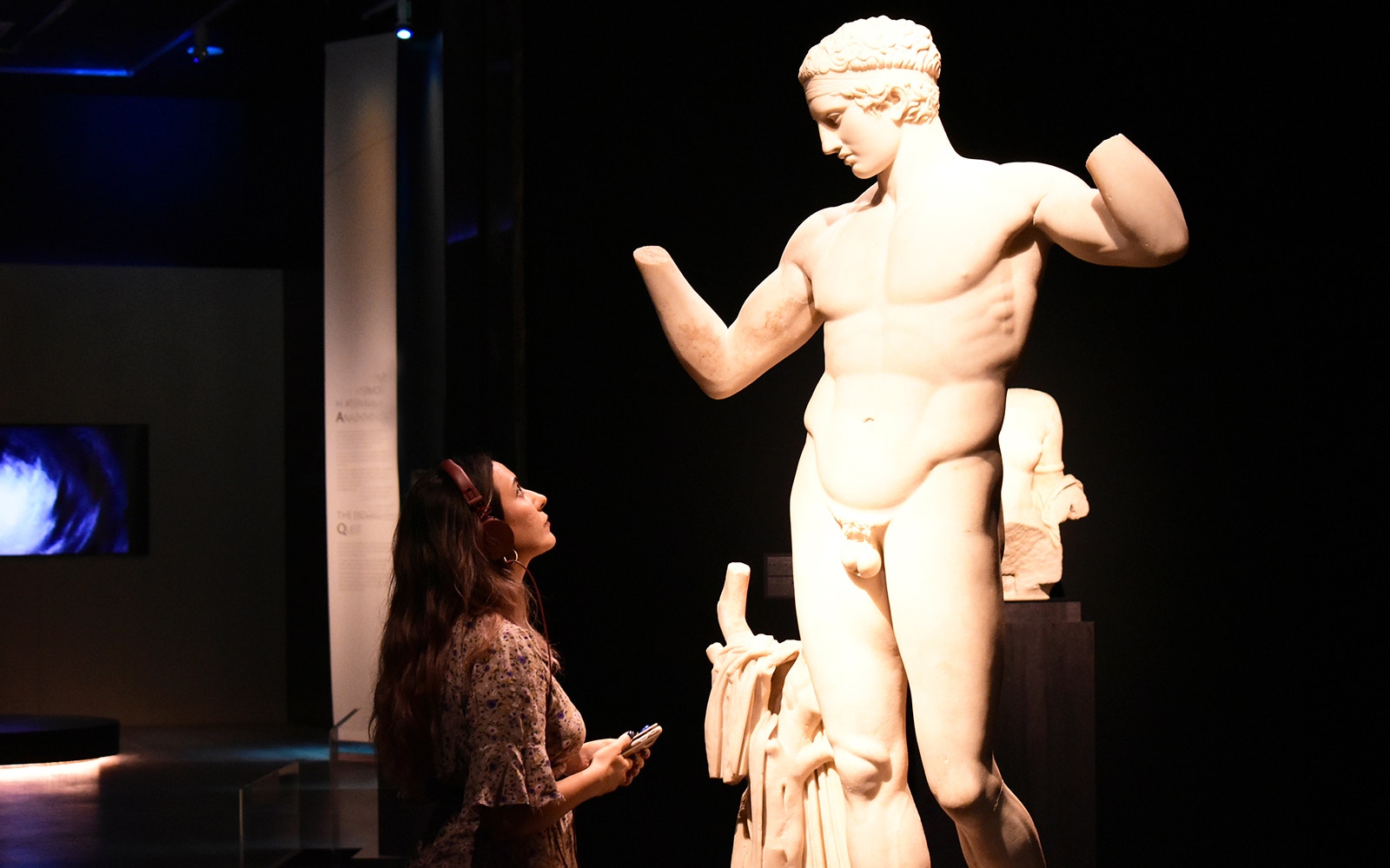 Visitor with audio guide admiring a classical statue at the National Archaeological Museum.