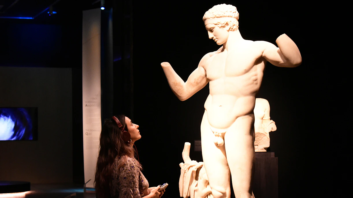 Visitor with audio guide admiring a classical statue at the National Archaeological Museum.