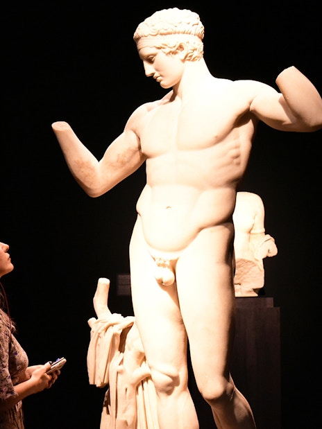 Visitor with audio guide admiring a classical statue at the National Archaeological Museum.