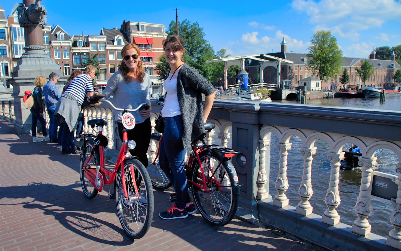 Two people with handbrake bikes on a bridge in Amsterdam, enjoying a full day bike rental.