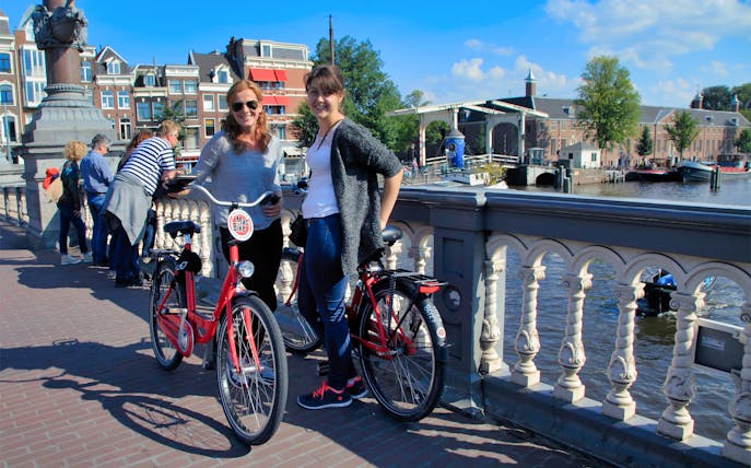 Two people with handbrake bikes on a bridge in Amsterdam, enjoying a full day bike rental.