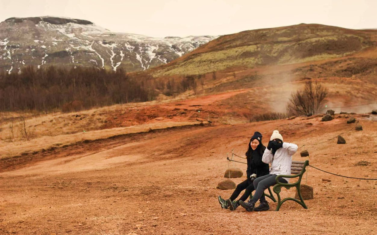 Visitors sitting on a bench with Icelandic geothermal landscape in the background during Golden Circle tour.