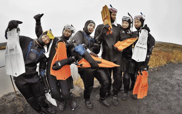 Group of snorkelers in wetsuits holding fins, preparing for Silfra snorkeling tour in Iceland.