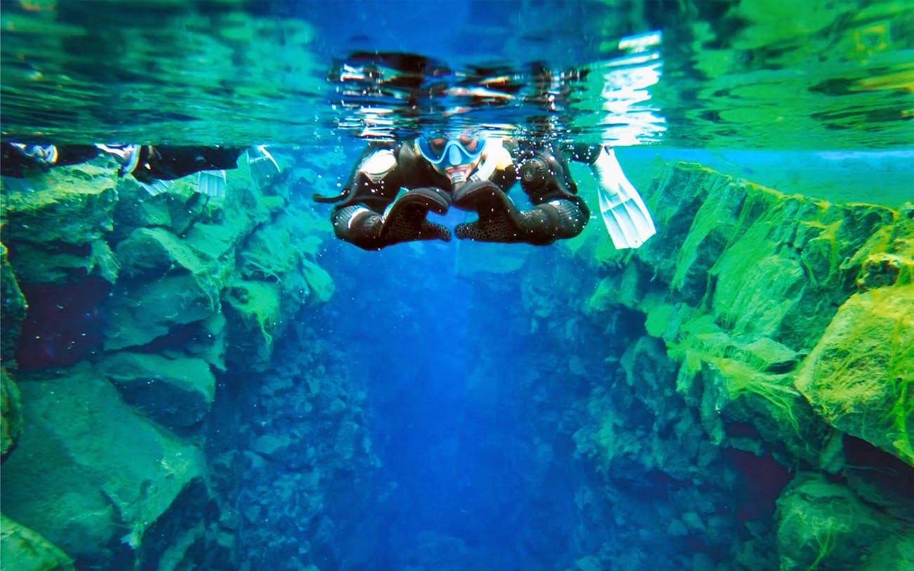 Snorkeler in Silfra fissure, Iceland, exploring clear blue waters and rocky formations.